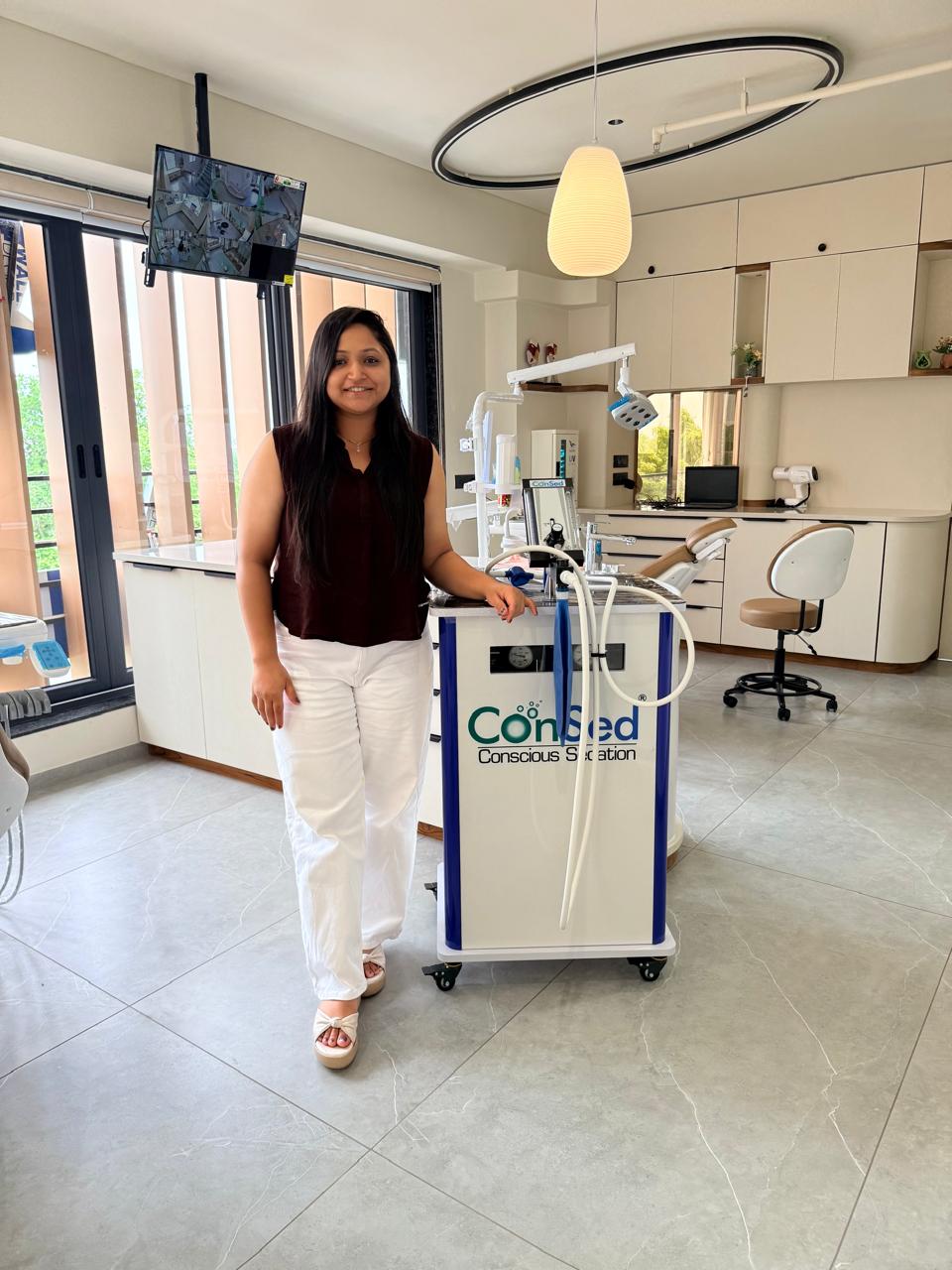Dr. Krishna Kotadiya Shah beside the ConSed nitrous oxide conscious sedation unit in an Aroma Dental Clinic treatment room